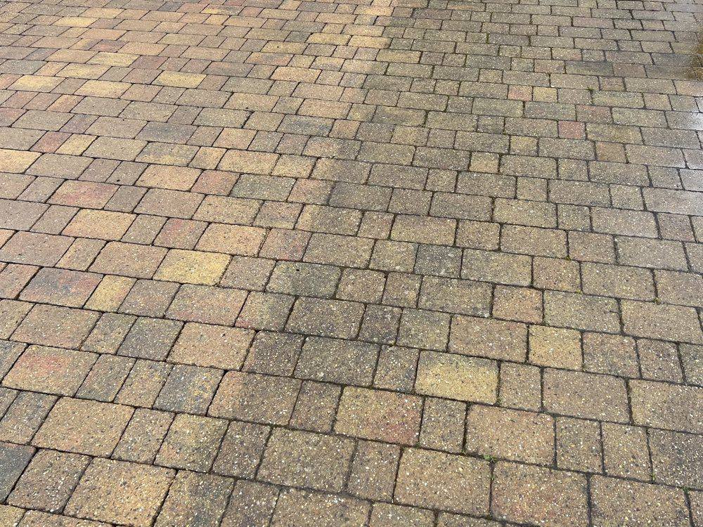 Block paving driveway mid-clean showing the washed side brighter than the weathered side