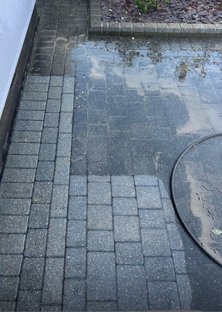 Charcoal block paving mid-clean, with the washed section noticeably brighter than the unwashed