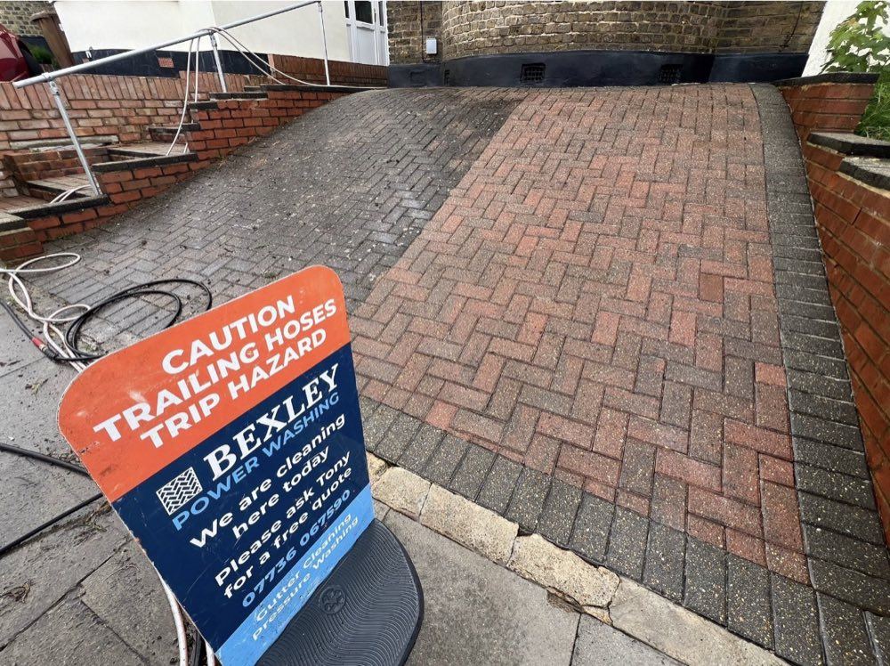 Sloped herringbone driveway half cleaned with a Bexley Power Washing caution sign in the foreground