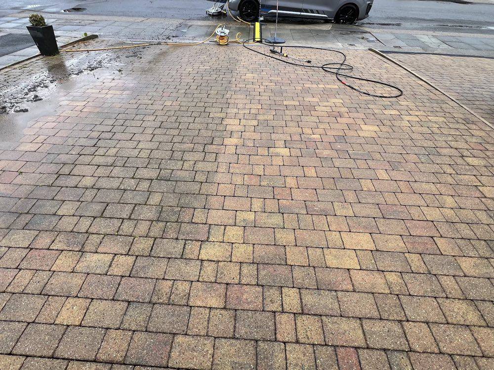 Large block-paved forecourt mid-clean with pressure washing equipment set up