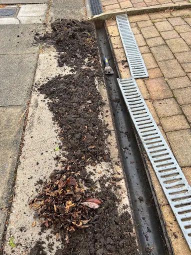 Driveway channel drain blocked with mud and leaves before gutter and channel cleaning