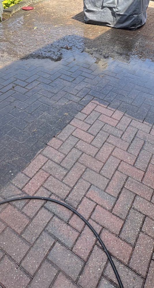 Red herringbone block paving mid-clean, washed bricks showing their colour against the dark unwashed area