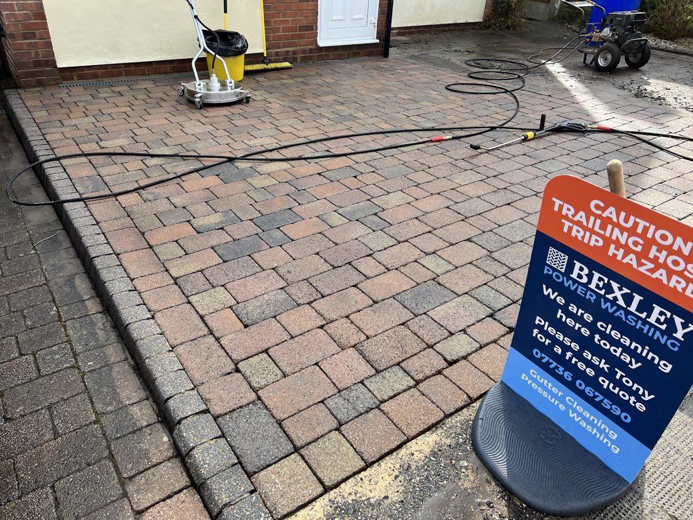 Rotary surface cleaner, pressure washer and Bexley Power Washing sign set up on a block paving driveway
