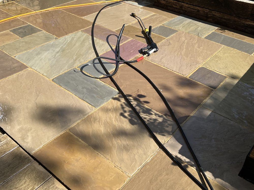 Pressure washing lance and hoses resting on a freshly cleaned sandstone patio in the sun