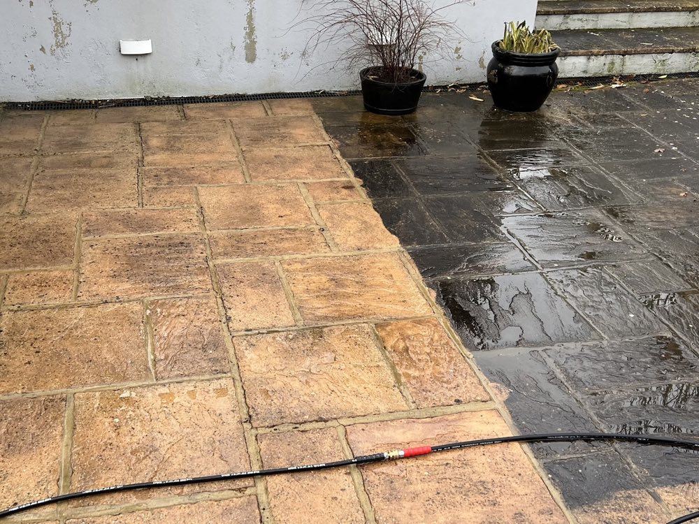 Riven patio slabs mid-clean, golden stone revealed next to the blackened unwashed side
